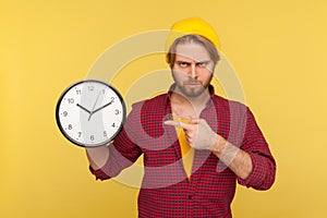 Look at time! Portrait of impatient angry hipster guy in checkered shirt pointing big clock and looking displeased