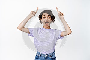 Look up ahead. Smiling happy brunette woman, young girl pointing fingers at top advertisement, promo sale upwards