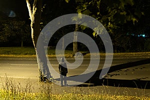 Lookig down on a mysterious hooded figure standing on a road. Underneath a tree at night