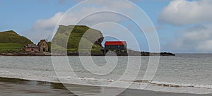 Looking across a bay at a boat house near to a large rock