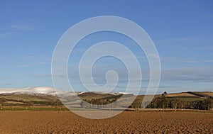 Looking across ploughed and grassy Fields between Drystone walls and onwards to the snow covered Hills.