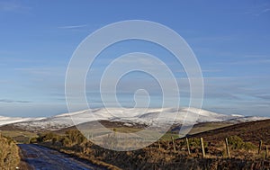 Looking across ploughed and grassy Fields between Drystone walls and onwards to the snow covered Hills .