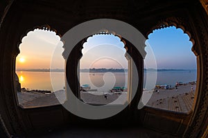 Looking through archway from majestic palace at Maheshwar, Madhya Pradesh, India. Ghats and holy Narnmada River at sunrise.