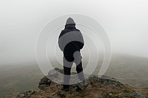 Looking at the back of a hooded figure looking out on a moody foggy winters day.