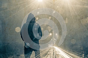 Looking at the back of a hooded figure looking out on a motorway and traffic trails on a moody foggy winters night. With light fla