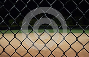Looking at a baseball field at night through the fence.