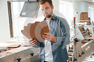 Looking at cardboards. Handsome man is working at the factory of creating eco boxes photo