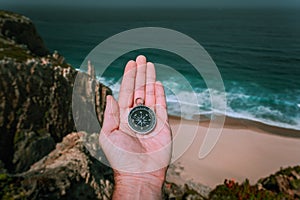 Looking at the compass in man hand palm symbolling adventure-seeking concept against sea and waves in coastline in