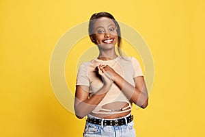 Looking delightful. Portrait of beautiful young african girl in casual clothes posing with smile against yellow studio