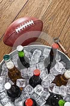 Looking down on an American football with a tub of assorted ice cold beer bottles on a wooden table