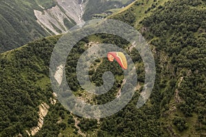 Looking down at a couple hang gliding high over the lower Caucasus mountains with cliffs and trees and a tiny river running far