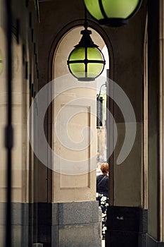 Looking down covered passageway next to contemporary luxury arcade building showing vertical lines, partial view of one person and