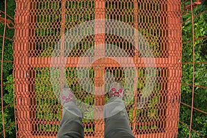 Looking down at hiking boots on a red suspension bridge