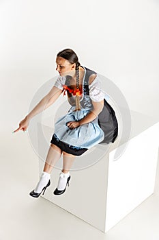 One pretty woman, waitress in traditional Austrian or Bavarian costume sitting on huge box isolated over white