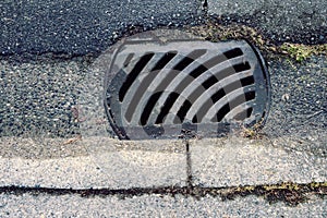 Looking down at a section of a street curb and storm drain