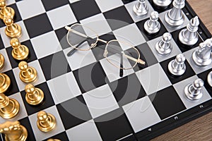 Looking down and shooting the facing chess pieces on the chessboard and a pair of glasses between the two sides