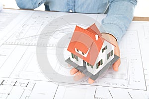 Looking down and shooting, the hard-working architect is holding a small house model and working against the drawings