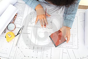 Looking down and shooting, the hard-working architect is holding a small house model and working against the drawings