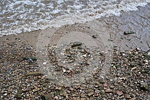 Looking down at small waves breaking on rocks and stones on river bank at low tide