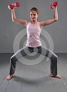 Looking down teenage sportive girl is doing exercises to develop with dumbbells muscles isolated on grey background. Sport healthy