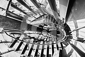 Looking down from the top of a circular staircase; bright light passing through the glass panels of the railing and creating