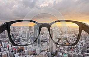 Looking through eyeglasses to city sunset view, focused on lens with blurry background