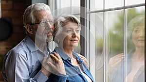 Elderly spouses hug look at window meet twilight years together