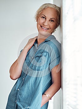 Looking good and loving life. Portrait of an attractive mature woman leaning against a wall at home.