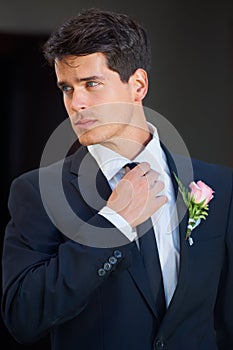 Looking great on his big day. A handsome groom wearing a pink rose on his jacket isolated on a black background.