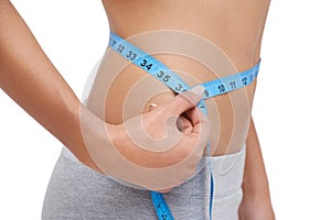 Looking great. Studio shot of a woman measuring her waistline.