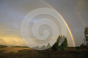 A bright rainbow over a field and copses after an autumn rain at sunset. Autumn bad weather in the foothills of the Western Urals.