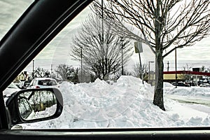 Looking out car window at piled up snow drifts and a convenience store in the distance with rear view window showing more snow