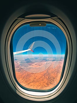 Looking out the window of an airplane flying over the dessert of Australia with bright blue summer sky