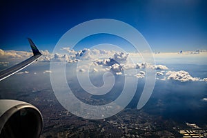 Looking out the window of an airplane to see a wingtip, engine and bright fluffy clouds and a deep blue sky photo