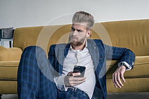 Looking perfect. Handsome young man in full suit using his cell phone while sitting on the floor at home