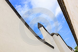 Looking skyward in a hutong alley between two white traditional brick concrete walls and tiles