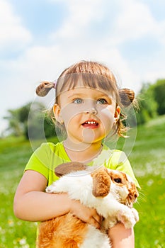 Looking small girl hugging rabbit in green field