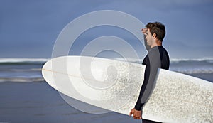 Looking, surfing and man with surfboard at beach for, waves on summer vacation, weekend and holiday by sea. Travel