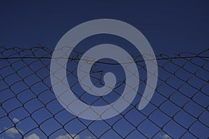 Looking up at a chain link fence with blue sky and clouds. wire fence. Chain link fence see sky. Opening in metallic fence. blue
