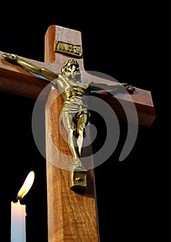 Looking up at crucifix isolated on black with burning white candle