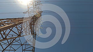 Looking up electric tower and power lines against sun, tilt up, rotate.