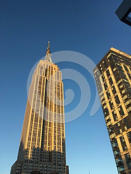 Looking up at the Empire State Building at the golden hour, warm light illuminates the iconic Art Deco skyscraper in midtown