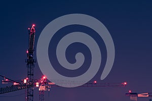 Looking up at group of tall and high tower cranes with red position lights at large construction site for housebuilding at night