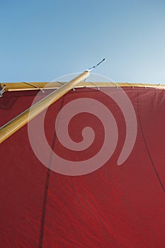 Looking up the rigging of a sailing dinghy: red sail, wooden mast