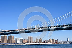 Looking up at the span section of Manhattan Bridge on a sunny day with blue sky. High-rise residential buildings behind the