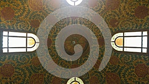 Looking up to a ceiling with oriental ornaments and colorful decorations of a dome with windows on the sides showing eastern