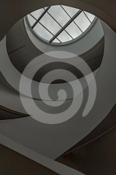 Looking up to the sky through modern channel round circular ceiling with spiral staircase