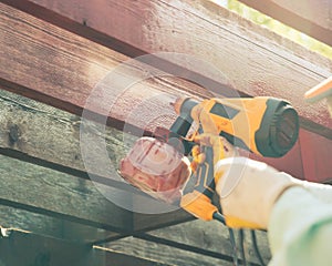 Looking up view Asian man hand using corded stain gun to repaint pergola timer wood outdoor structure in redwood color,