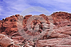 Looking upward at a cliff of jagged, craggy rocks with a blue, cloudy sky in the background. Red Rock, Nevada.