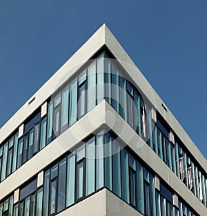 Looking upwards view of a corner of a modern angular concrete high white office building with bright blue lear sky